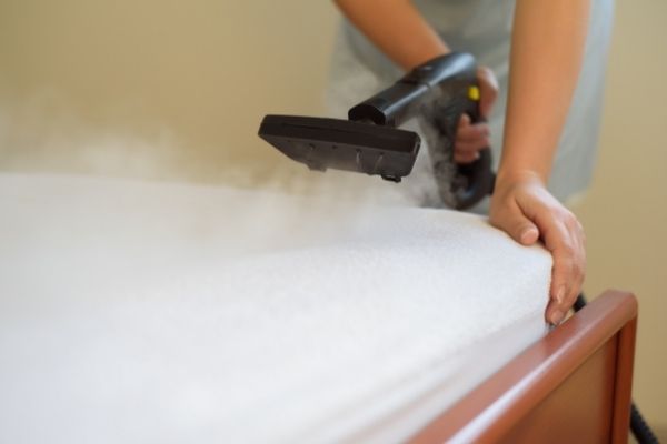 Person steam cleaning a mattress