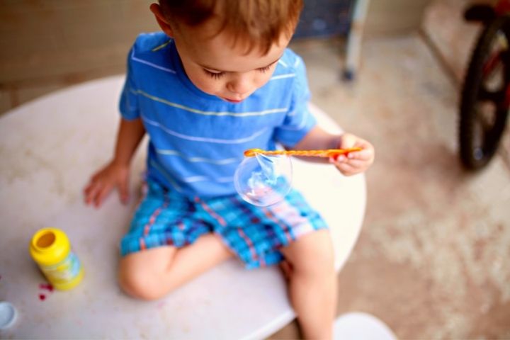 A Boy Sitting On A Carpet Inflates A Soap Bubble