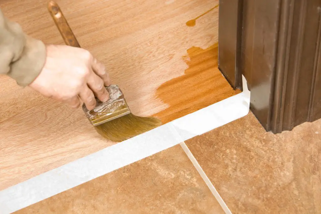 Painter Brushing Clear Polyurethane On Hardwood Floor